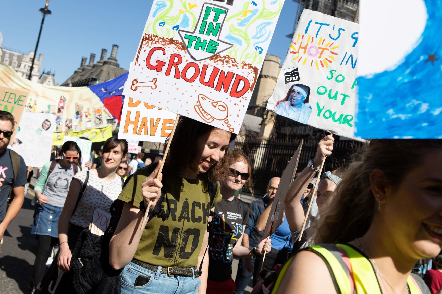 A young woman wearing a 'Frack No' t-shirt holds a banner in a protest march