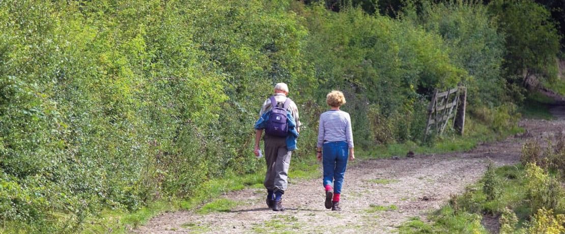 A couple pass a hedgerow whilst hiking in the Peak District