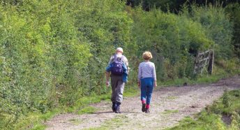 A couple pass a hedgerow whilst hiking in the Peak District