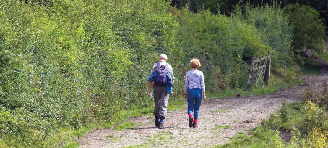 A couple pass a hedgerow whilst hiking in the Peak District