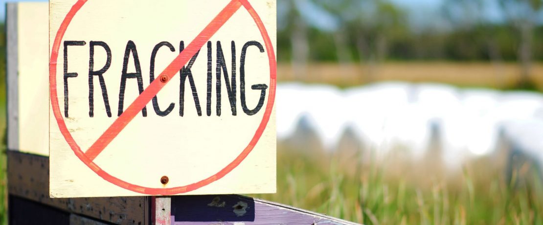 A wooden hand-painted sign with the word 'fracking' with a line through it