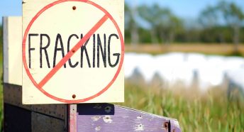 A wooden hand-painted sign with the word 'fracking' with a line through it