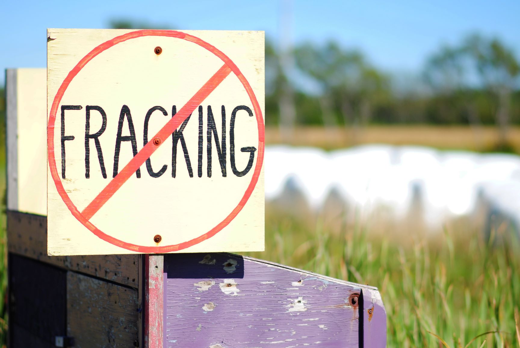 A wooden hand-painted sign with the word 'fracking' with a line through it