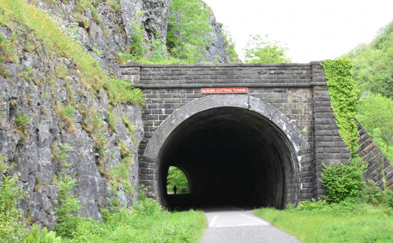 A path running through a long railway tunnel, in darkness with a figure silhouetted at the end