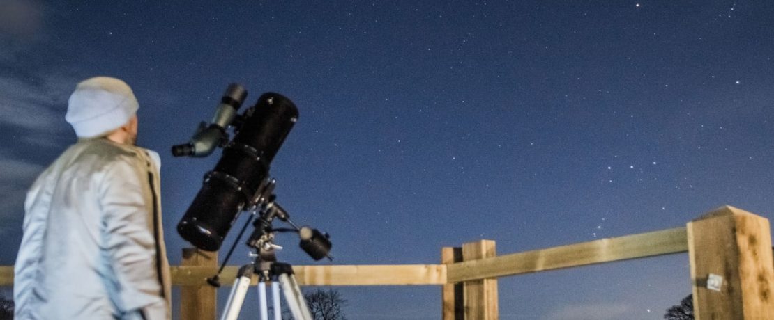 A man practising astronomy, with his telescope, with Orion visible in the background