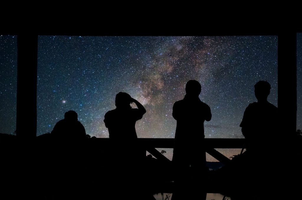A dark starry night sky with people silhouetted in the darkness in the foreground
