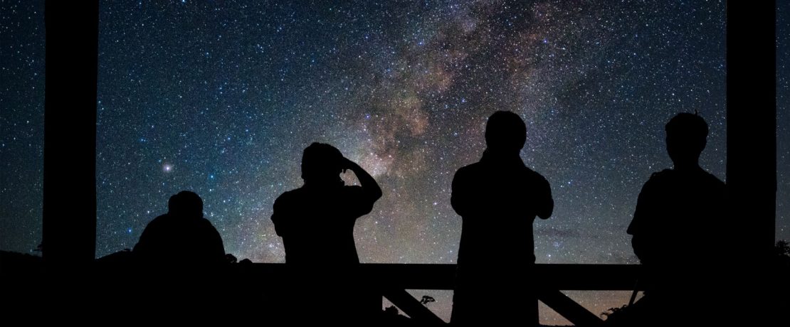 A dark starry night sky with people silhouetted in the darkness in the foreground