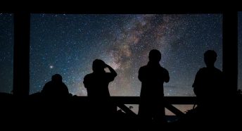 A dark starry night sky with people silhouetted in the darkness in the foreground