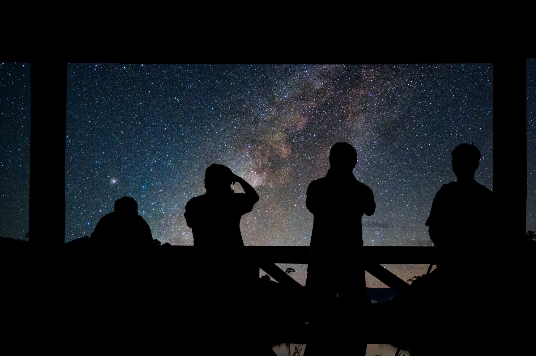 A dark starry night sky with people silhouetted in the darkness in the foreground