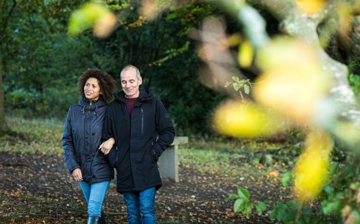 A couple walk arm in arm through woods