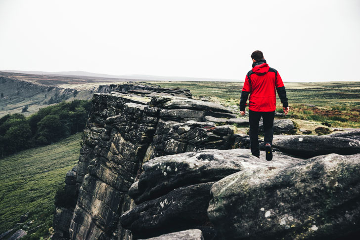 A man in a bright red jacket stands on the edge of a cliff