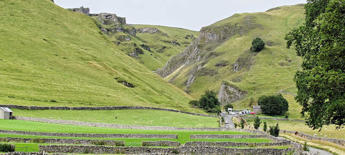 A view of English farmland down a valley with green grassy slopes and a farm