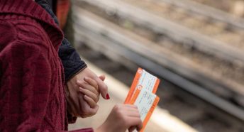 A detail of a woman holding a child's hand; the child holds train tickets