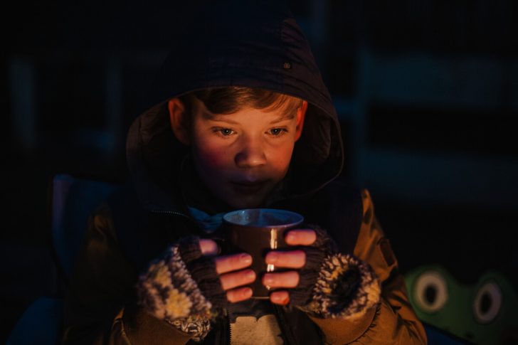 A young boy holds a mug in gloved hands