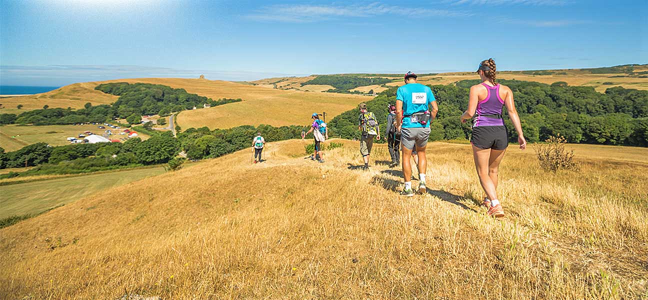 A row of people in shorts and t-shirts walk down a grassy path in bright sunshine