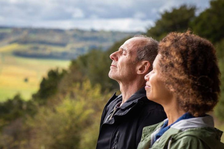 A man and a woman in the countryside with eyes closed, enjoying light on their faces