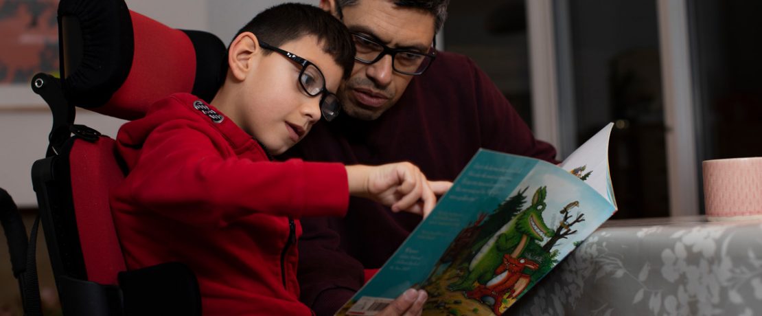 Man and boy reading a picture book inside a home at a table