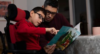 Man and boy reading a picture book inside a home at a table