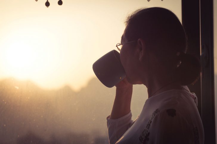 Woman drinking tea while admiring view from window