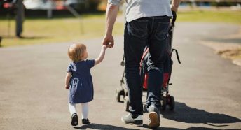 A man walks with a buggy on a path, holding a small girl by the hand