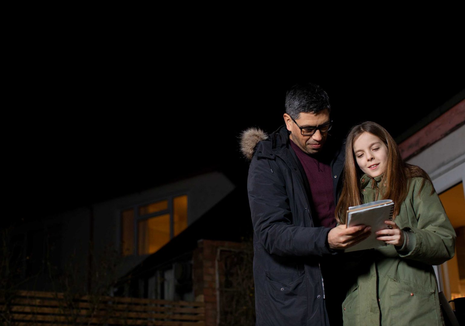 A man and young girl in a darkened garden with a notepad and pen