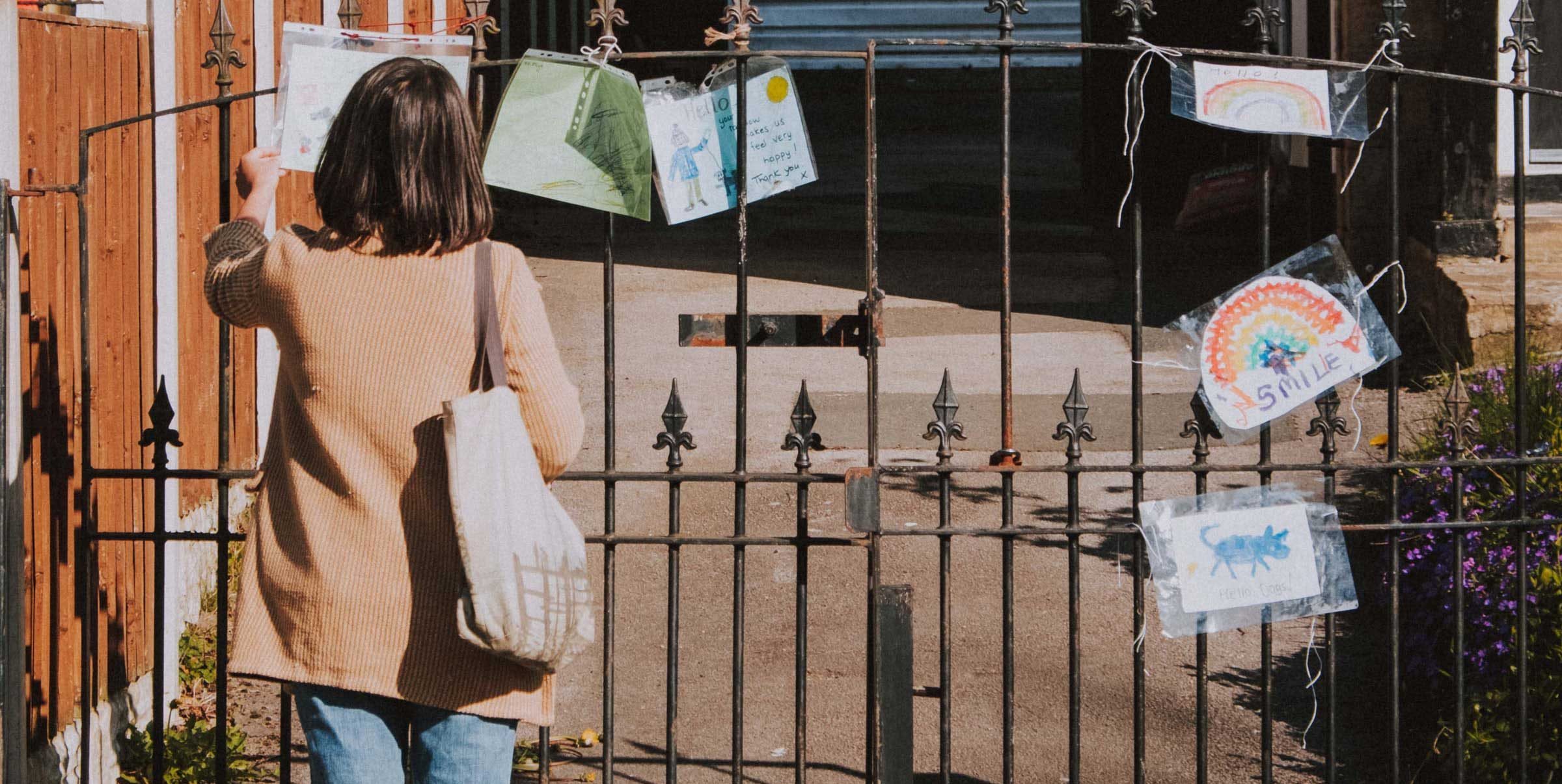 A woman reads signs left hanging on a fence with images of rainbows