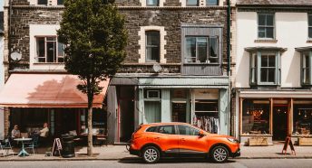 A high street with a car parked, a shop and cafe with people eating outside