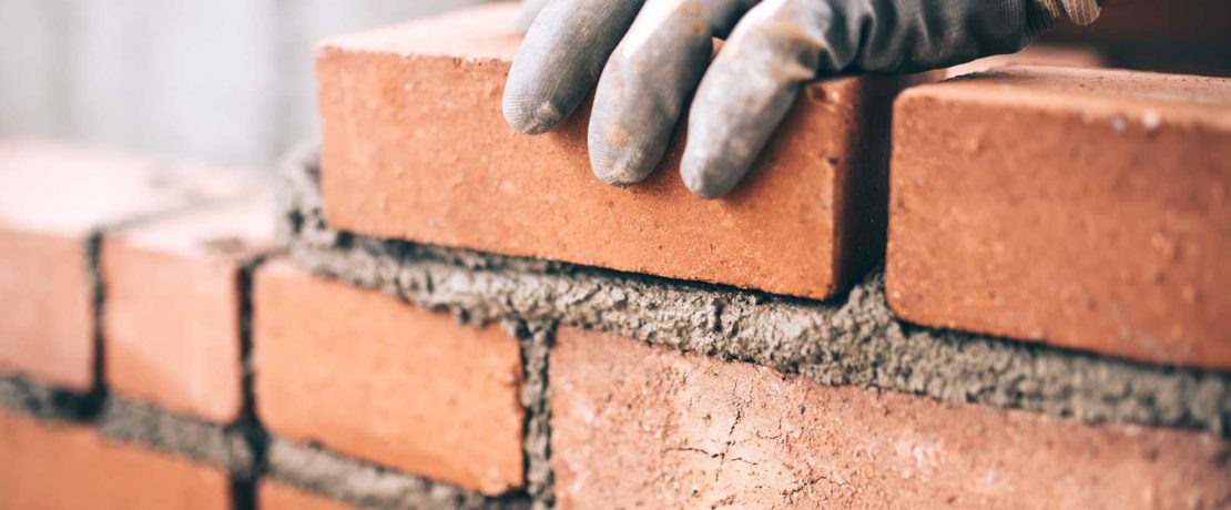 A gloved hand laying cement between red bricks