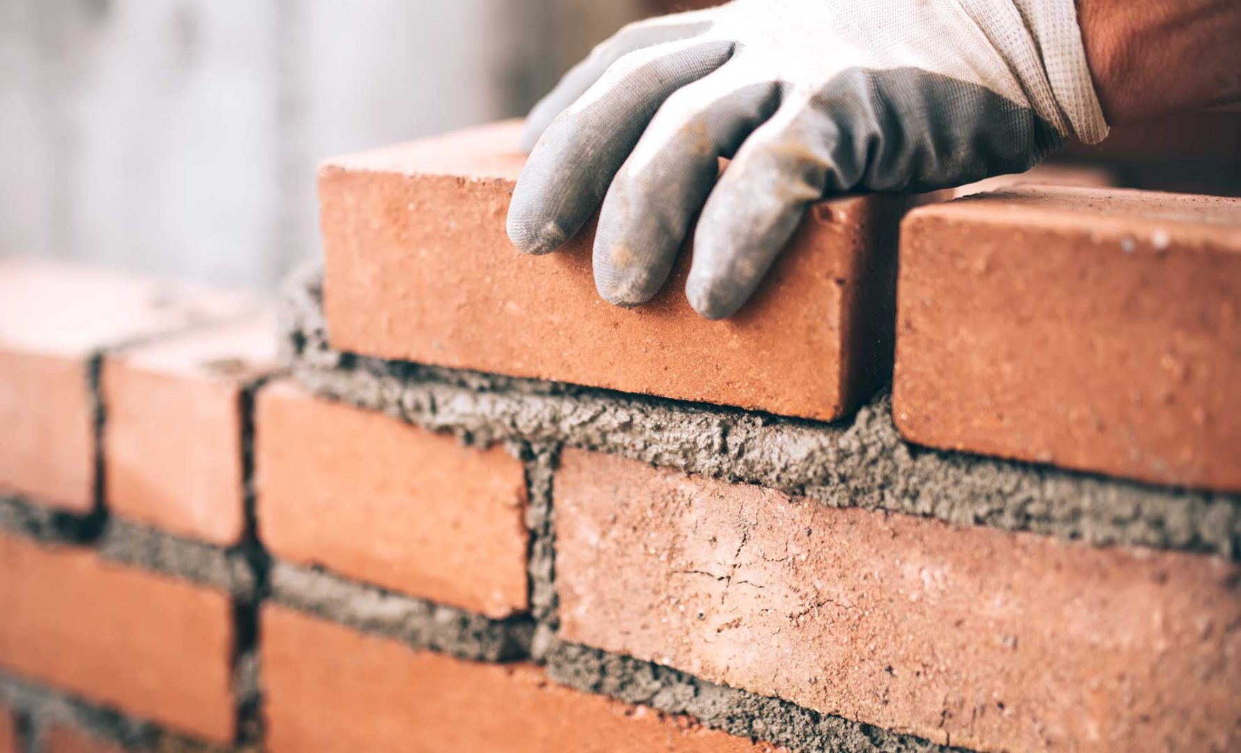 A gloved hand laying cement between red bricks