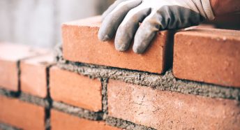 A gloved hand laying cement between red bricks