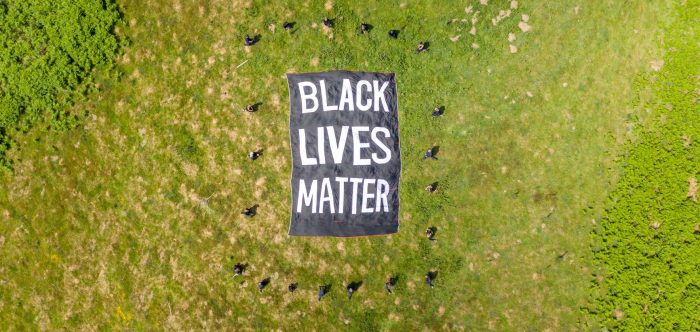 Black Lives Matter banner unfurled on grass with people surrounding it