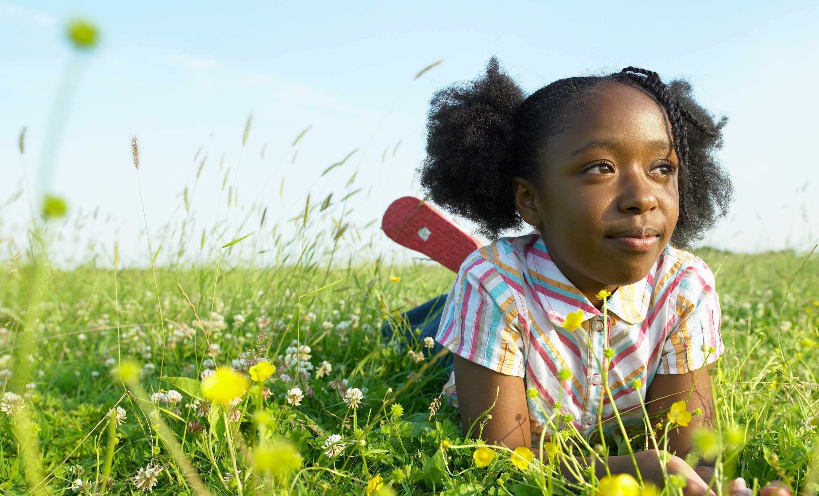 A girl in a colourful summer dress lying in a grassy field