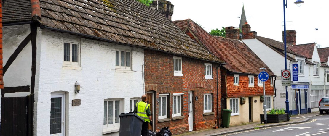 A refuse collector pulls a wheelie bin along a village street