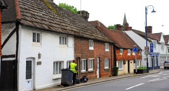 A refuse collector pulls a wheelie bin along a village street
