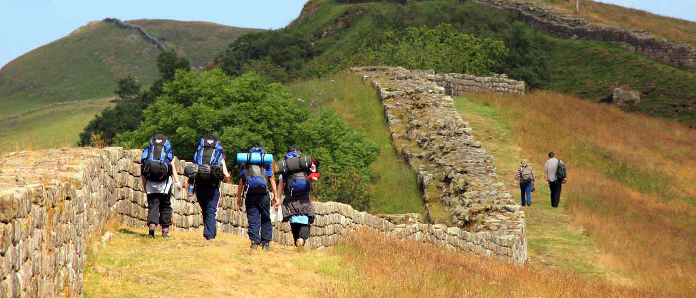 Hikers walk in a field beside Hadrian's Wall