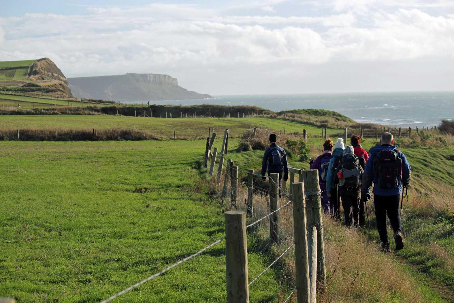 Hikers walk along the Jurassic Coast with the sea and cliffs in the distance