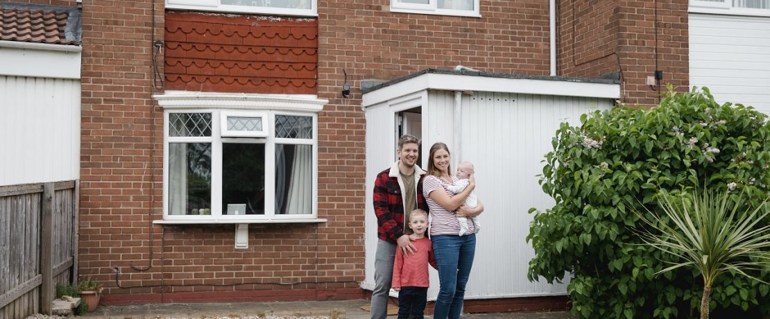 Family standing in front of house and smiling