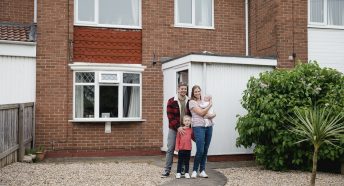 Family standing in front of house and smiling