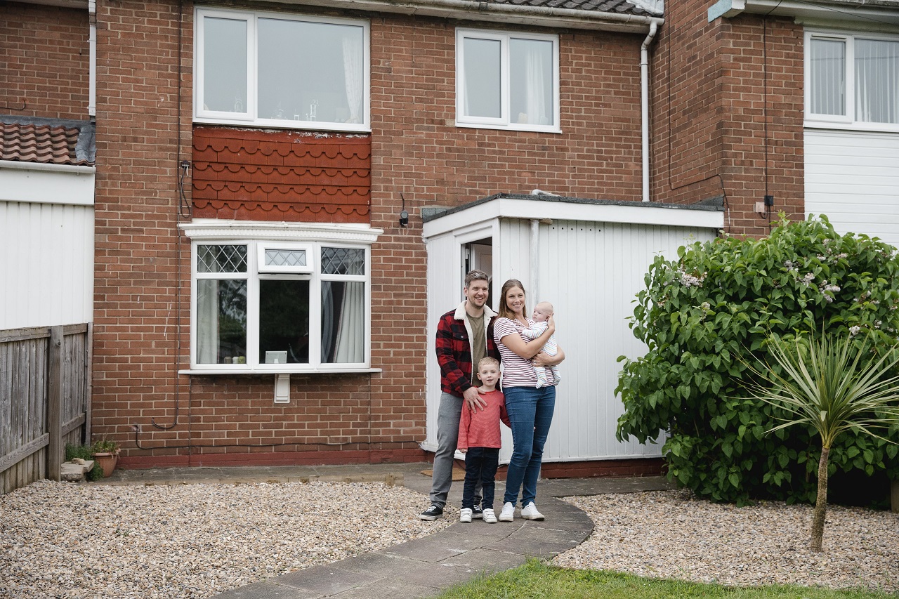 Family standing in front of house and smiling