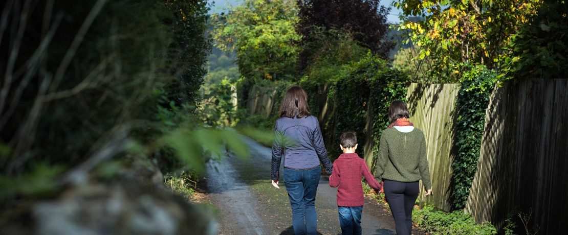 A family with two mothers and a small boy walk on a country lane