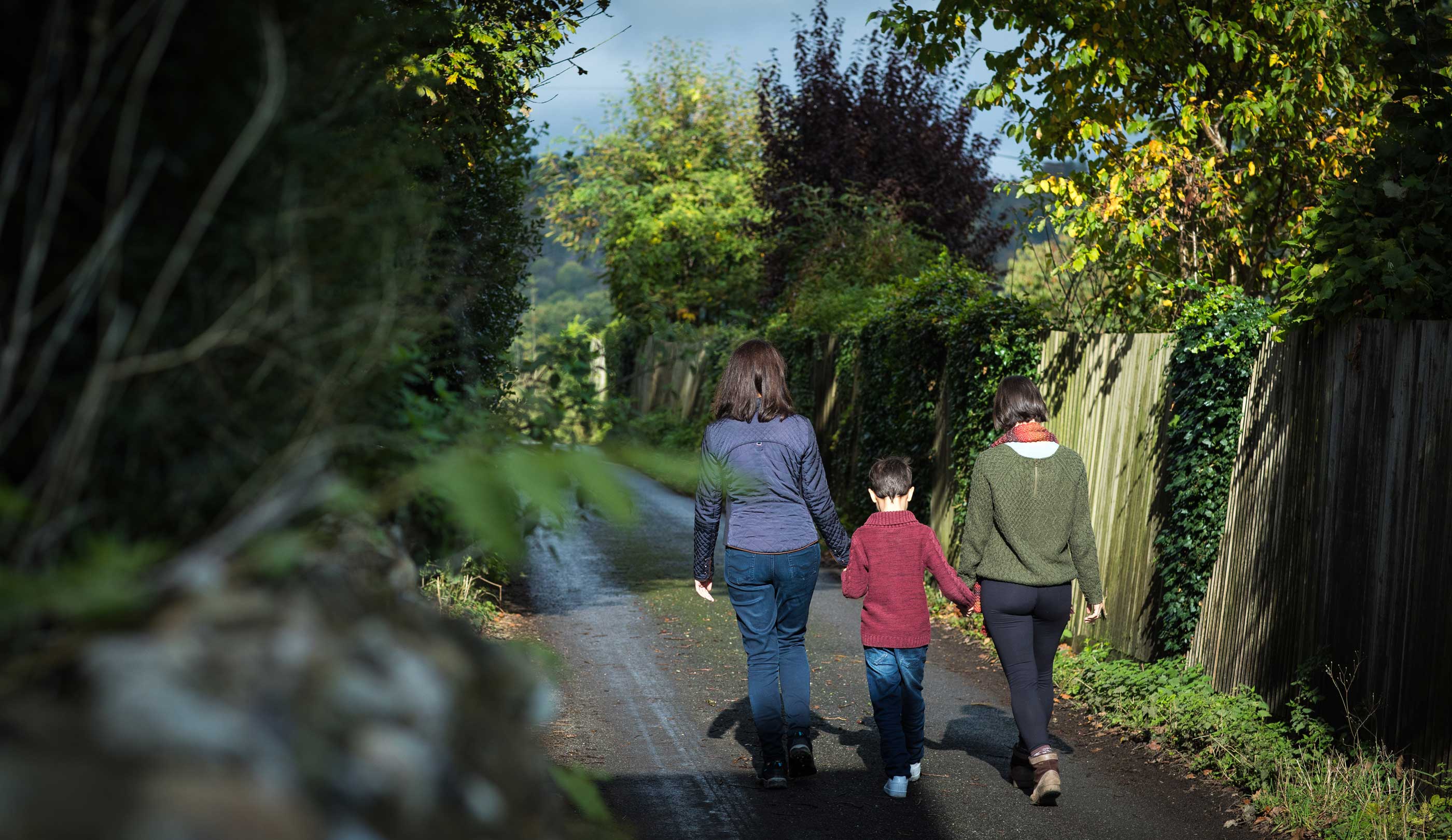 A family with two mothers and a small boy walk on a country lane