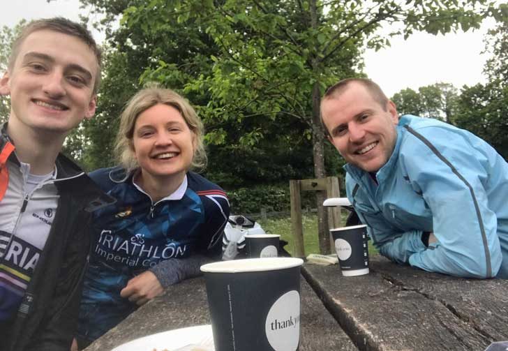 Three people at a picnic bench with coffee cups