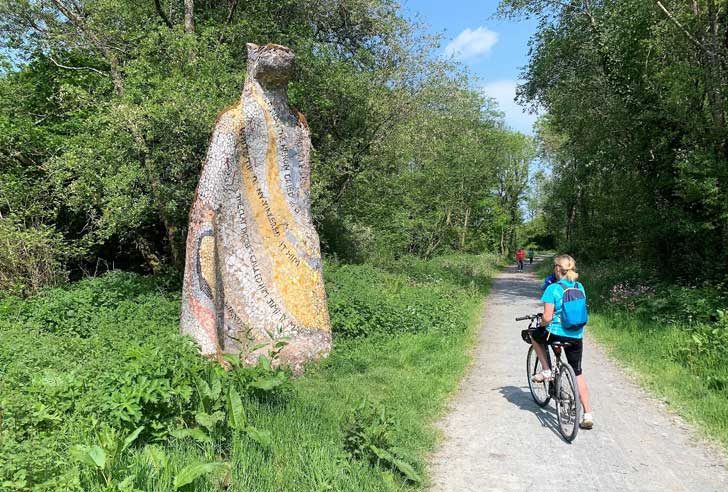 A woman on a bike stops to admire a sculpture beside the path