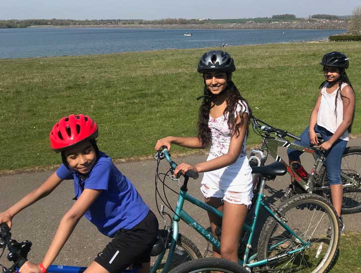 Three children pose on bikes on a coastal path