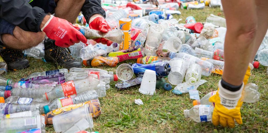 Two people bending to sort soiled plastic bottles on the grass