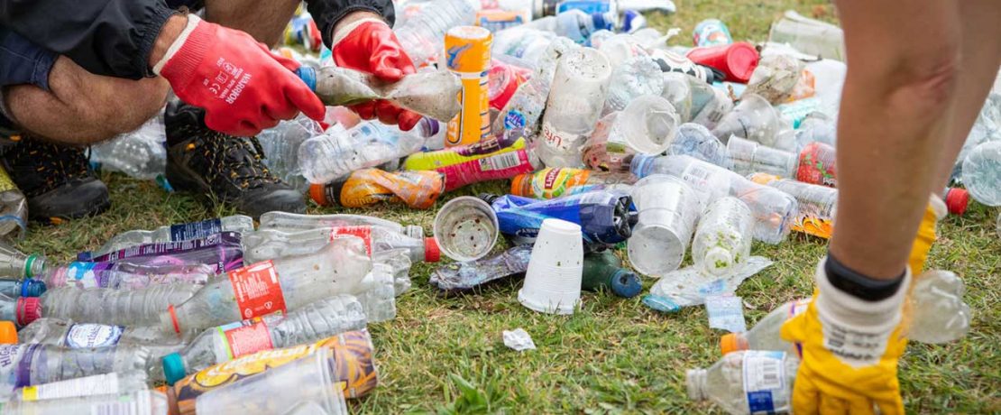 Two people bending to sort soiled plastic bottles on the grass