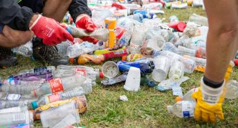 Two people bending to sort soiled plastic bottles on the grass