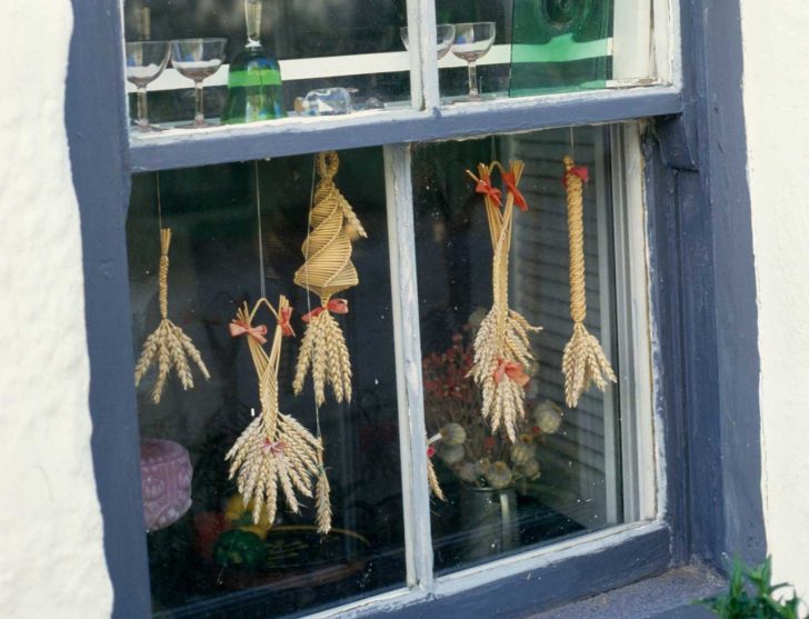 Corn dollies of various styles hanging in a window