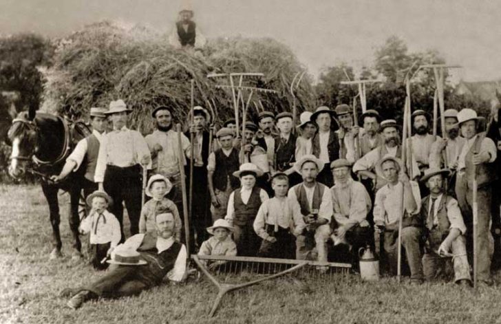 A black and white vintage shot of 28 people standing in front of a cart of hay
