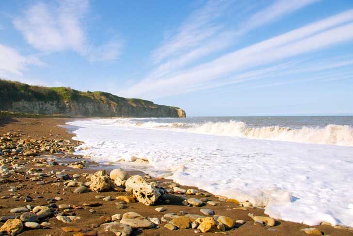 Waves rushing back over golden sand under blue sky with pebbles in foreground